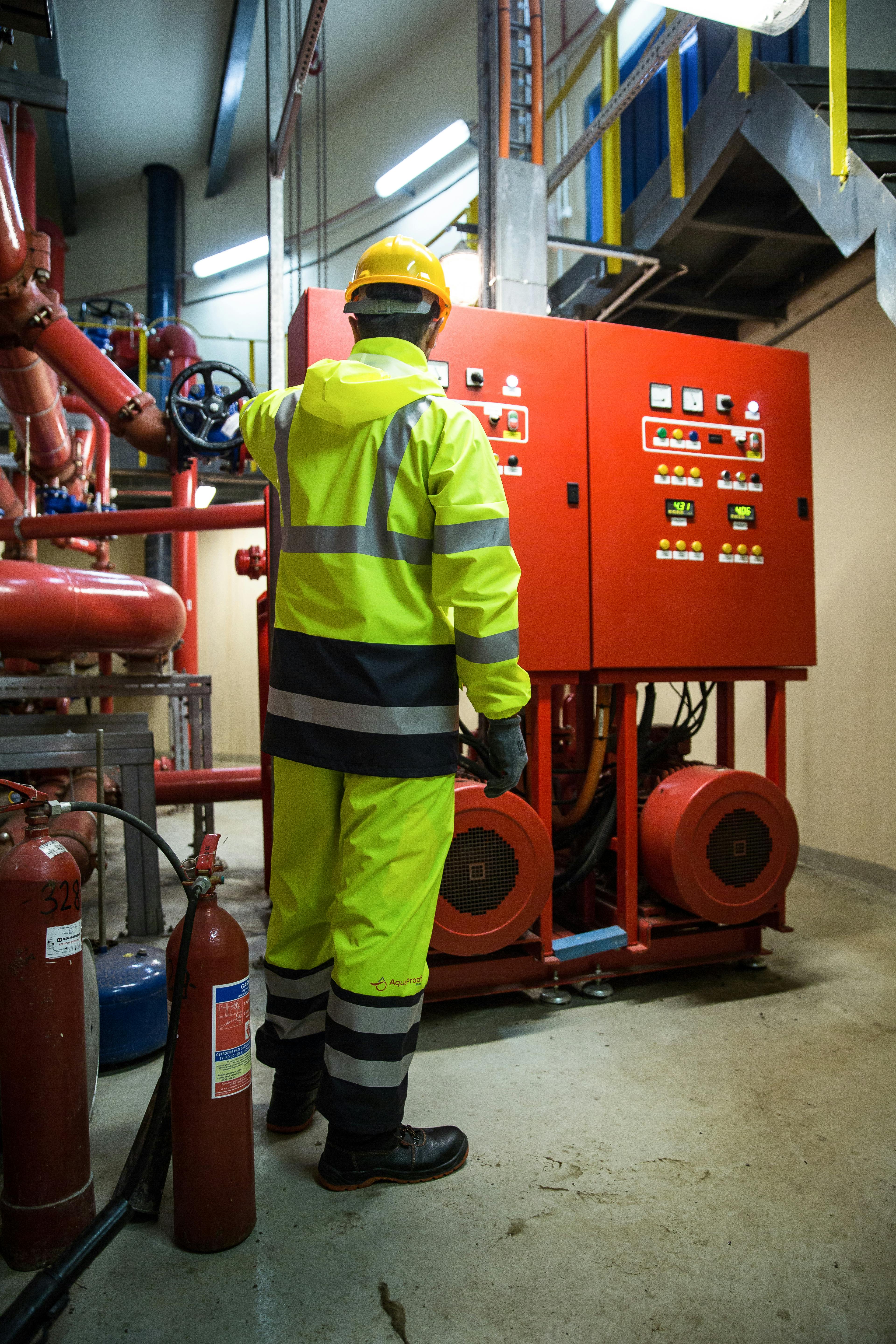 Engineer in high-visibility uniform operates control panel in industrial setting.