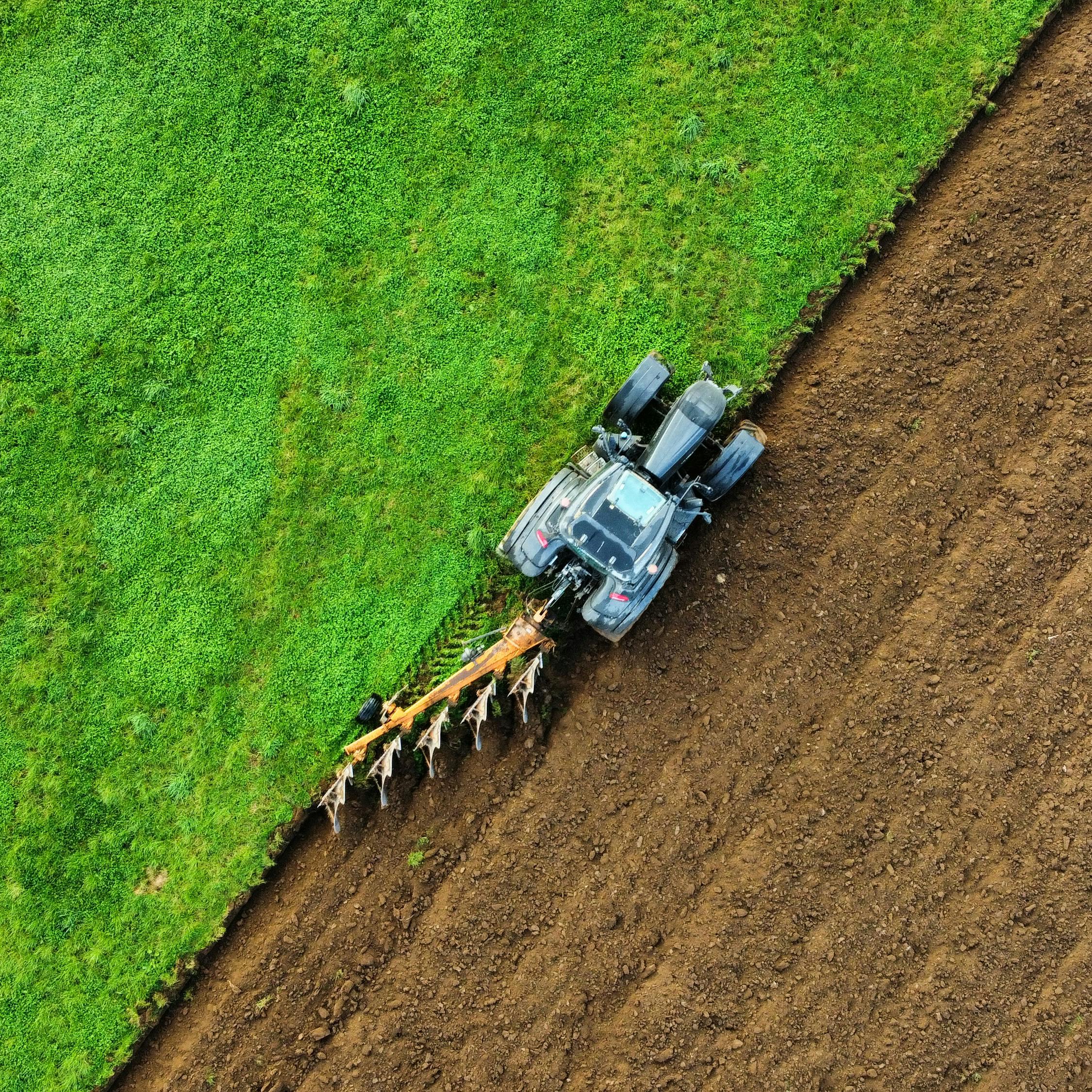 Aerial view of a tractor plowing a green and brown field from above.